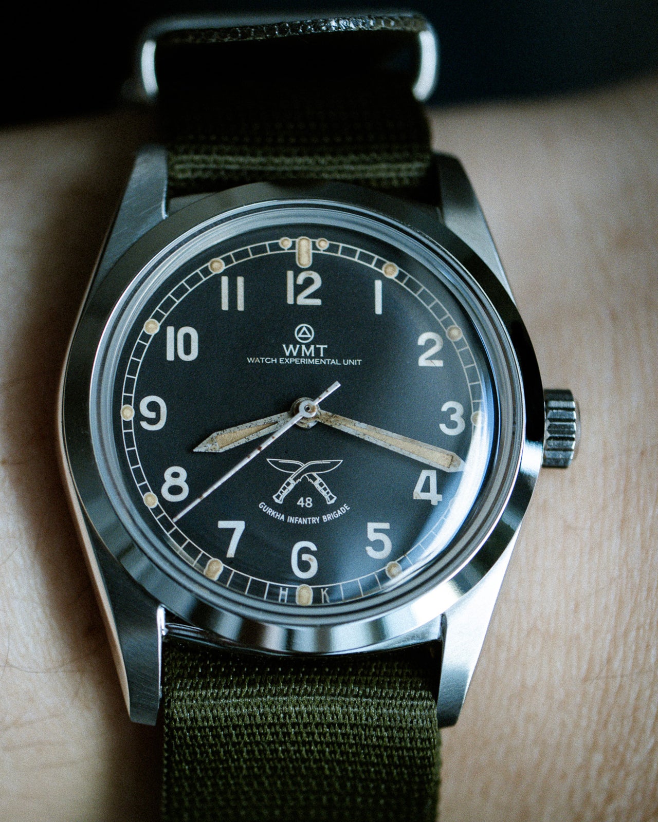 Wristwatch with green strap and black dial on a wooden surface