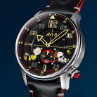 Close-up of AVI-8 Snoopy wristwatch with a black leather strap, silver-tone case, and a black dial featuring Charlie Brown, Snoopy and Woodstock cartoon characters
