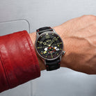 Wrist shot of AVI-8 Snoopy watch with a black dial, silver-toned case, and black leather strap