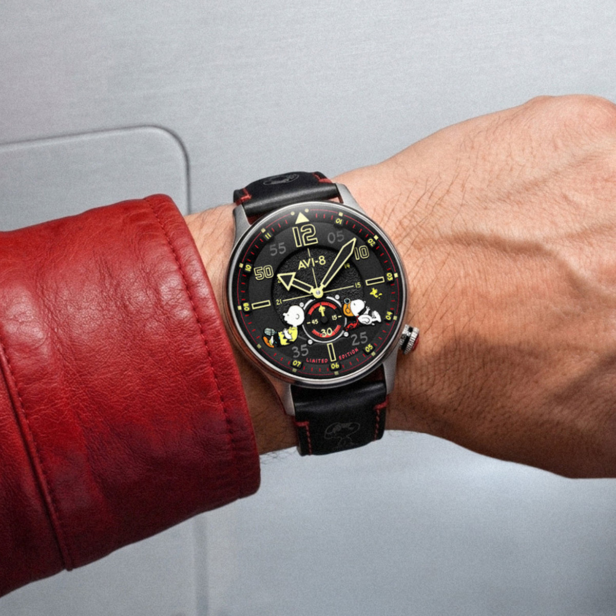 Wrist shot of AVI-8 Snoopy watch with a black dial, silver-toned case, and black leather strap